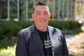 A man in a grey suit jacket smiles at camera