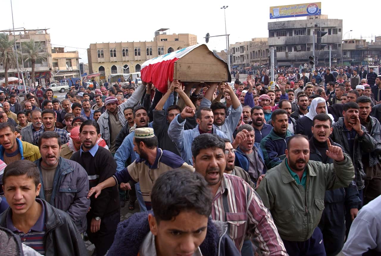 A crowd of people on the streets. Some are carrying a coffin.