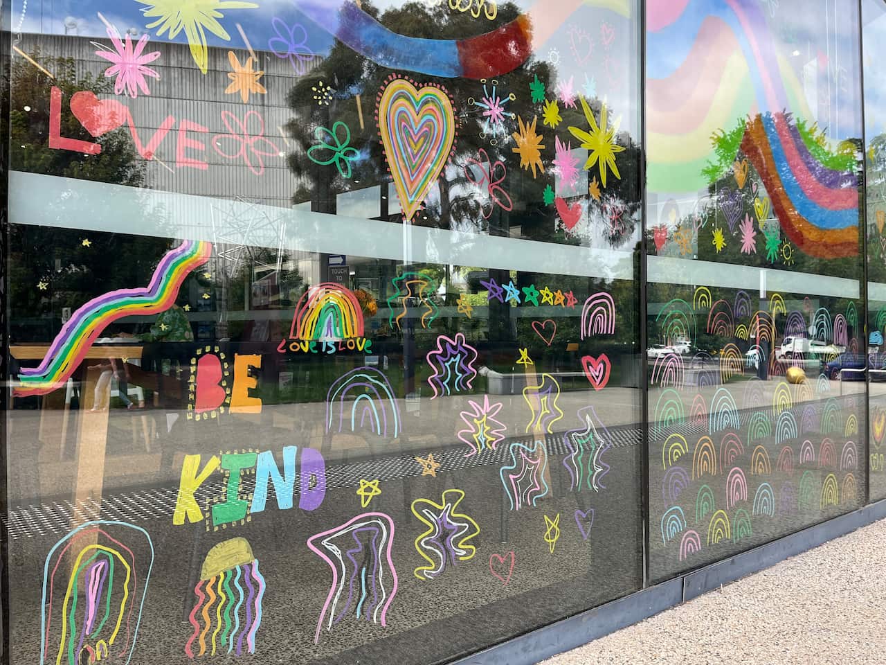 A set of glass window panes covered in colourful drawings, including rainbows, the words, 'BE KIND,' and love hearts.