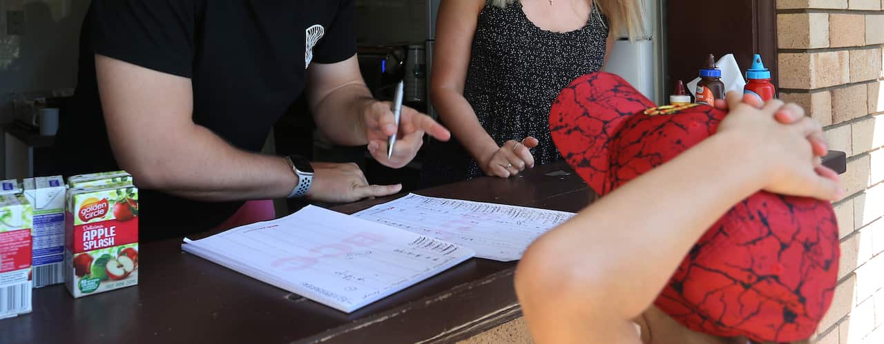 A child at the counter of a canteen being served by two adults.