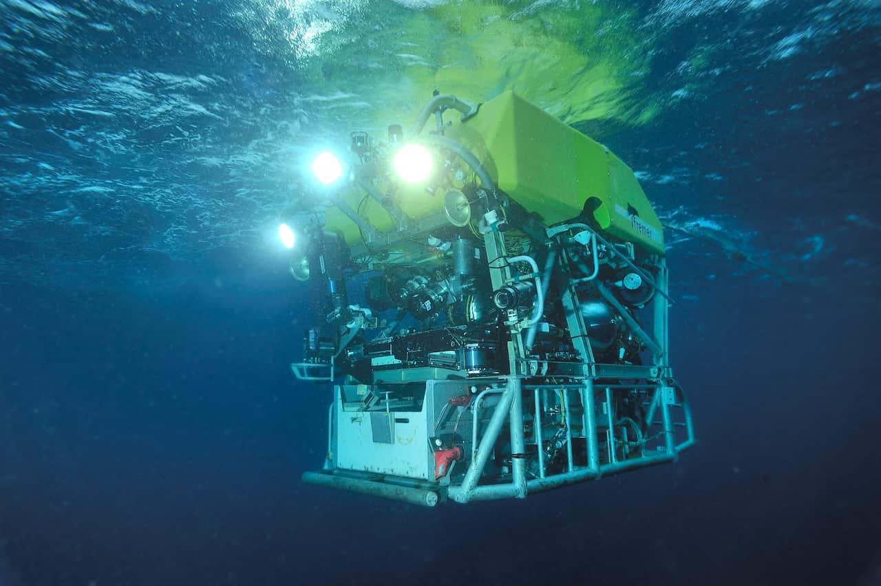 An undersea robot pictured underwater with headlights on.