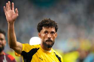 Vozinha holds his hand up high wearing a yellow and black goalkeeper kit.