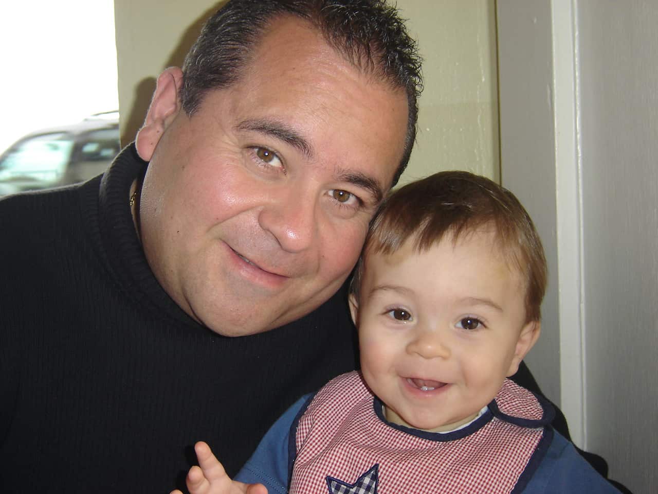 A man in a black shirt is smiling next to a baby boy.