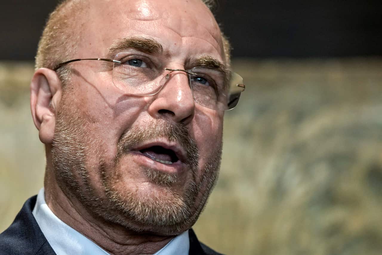 A headshot of a man in a suit delivering a speech.