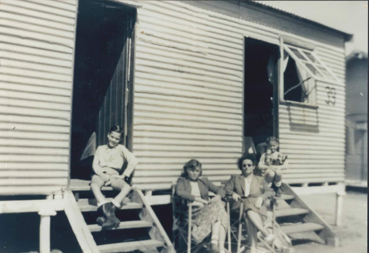 A black and white photo of two women sitting in chairs outside a building, with two children sitting on steps