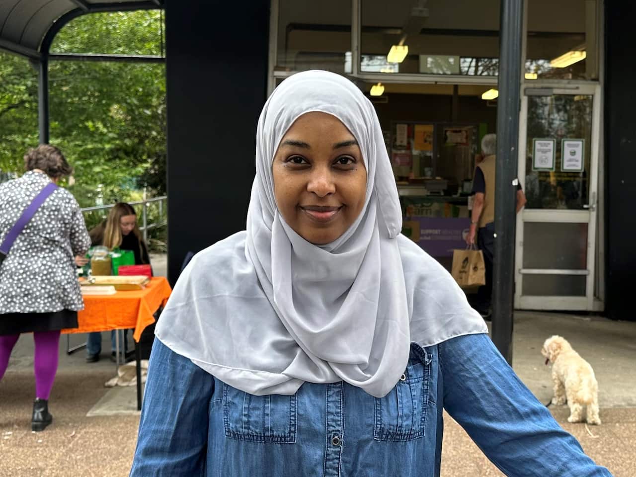 A woman of African heritage, wearing a light grey headscarf and denim shirt