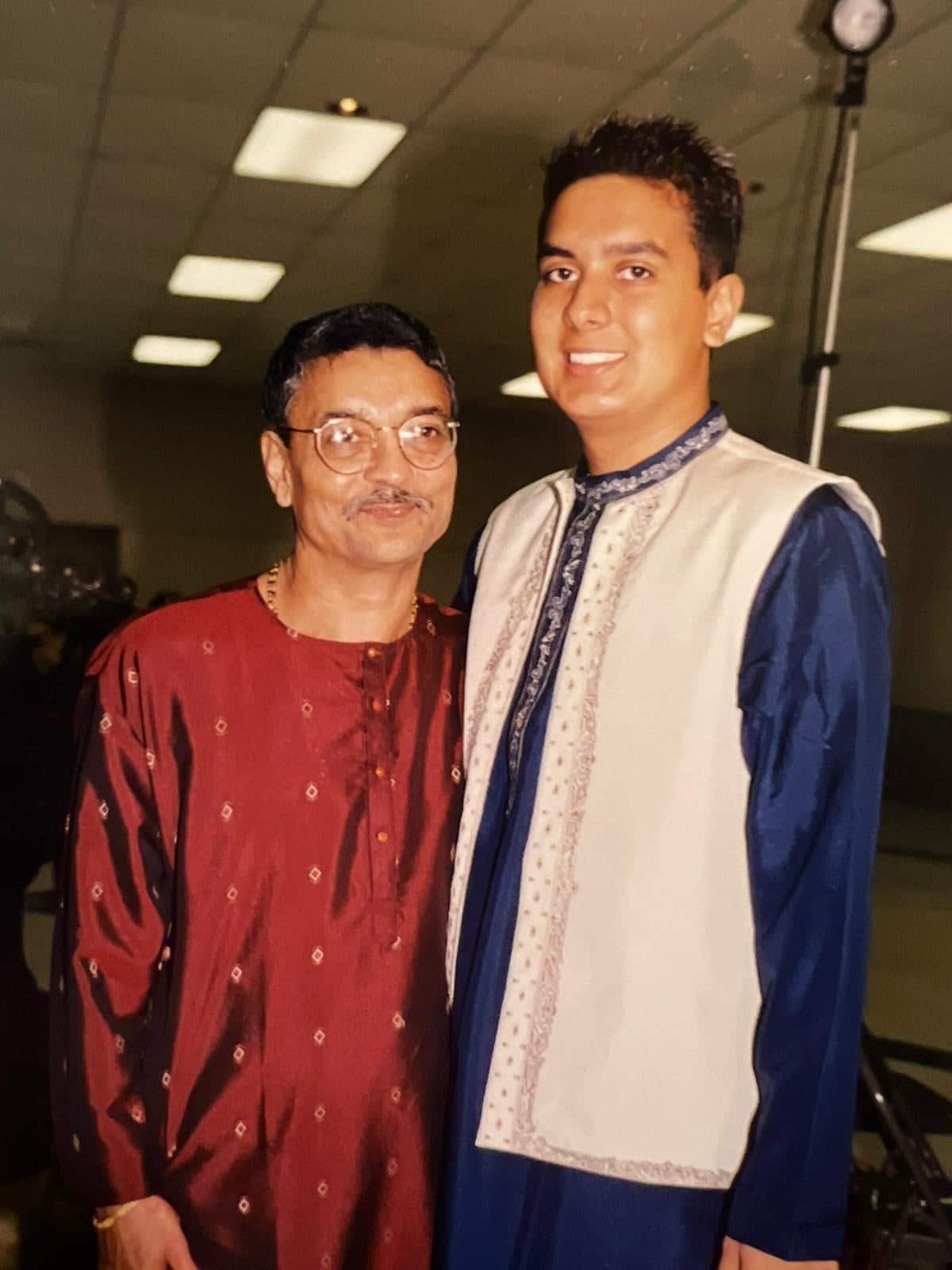 A young man stands next to his father, with both of them smiling for the camera.