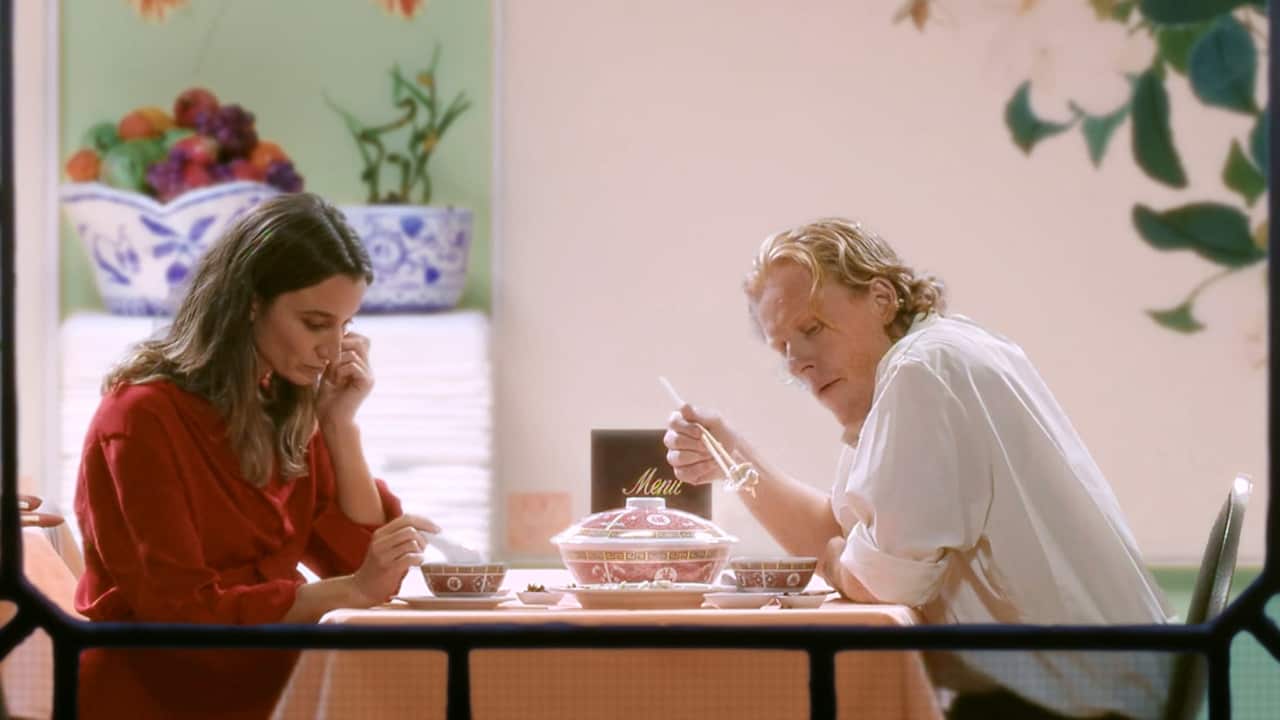 A man and a woman are siting at a table in a restaurant, with food bowls in front of them. 