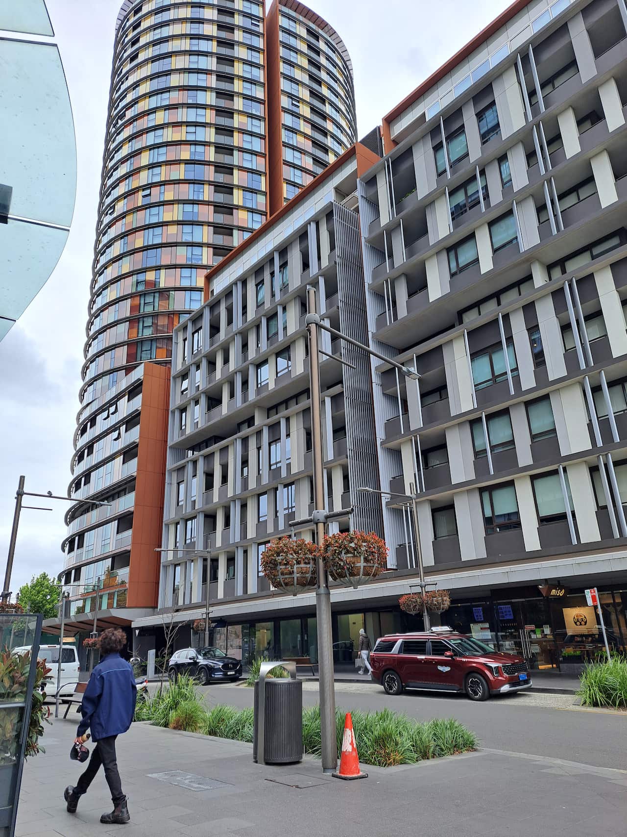 A pedestrian walks along a road next to large high rises. 