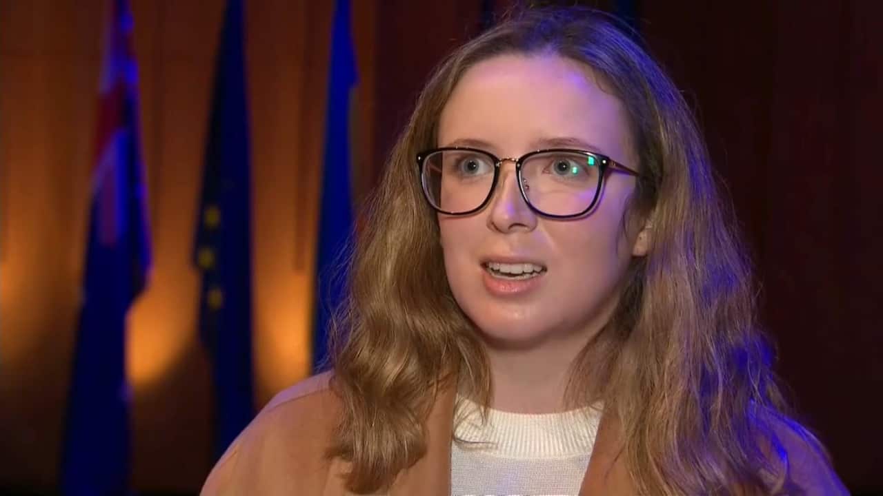 ANU student Olivia Claire Martin in a brown overcoat answers questions from SBS reporter Naveen Razik.