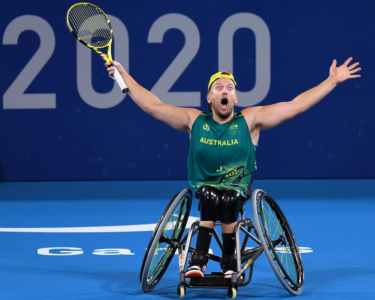 A man in a wheelchair cheers as he holds a tennis racquet.