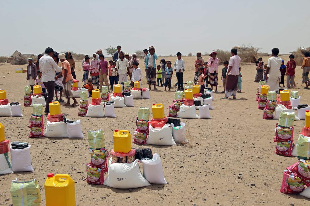 People standing on arid ground in Yemen, with food parcels in the foreground