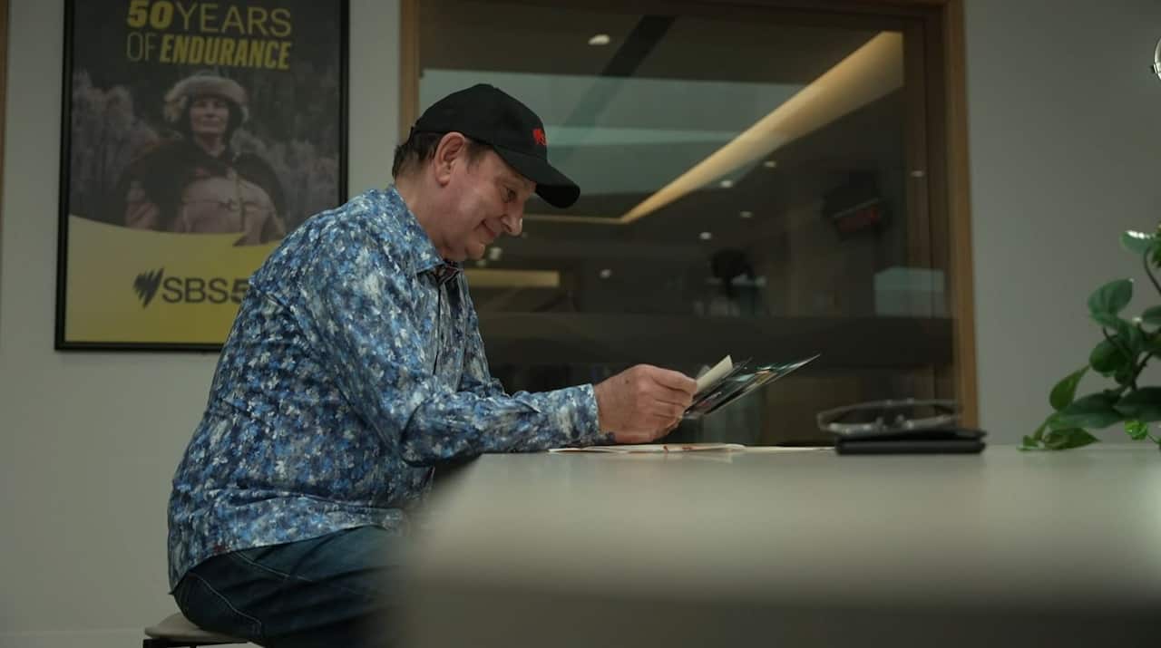 A man smiling as he looks at photos while sitting at a table.