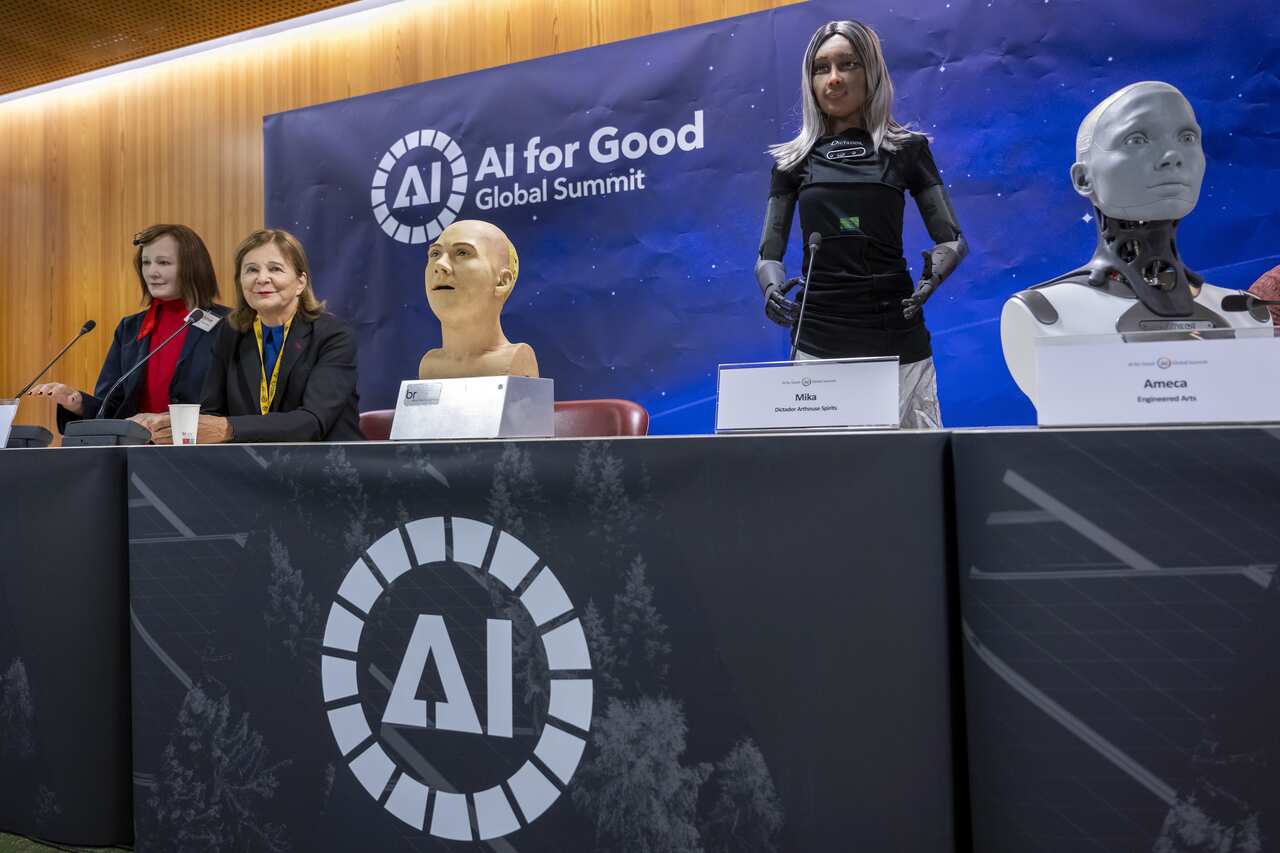 Lifelike humanoid robots speak during the world's first press conference as two people sit at the table.
