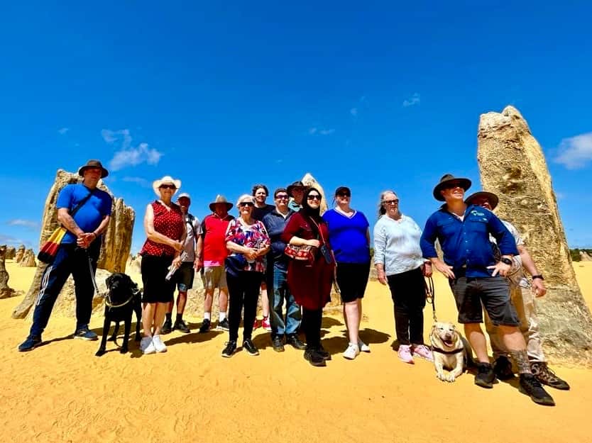 A group of 12 low-vision travellers are posing for photos in the desert.