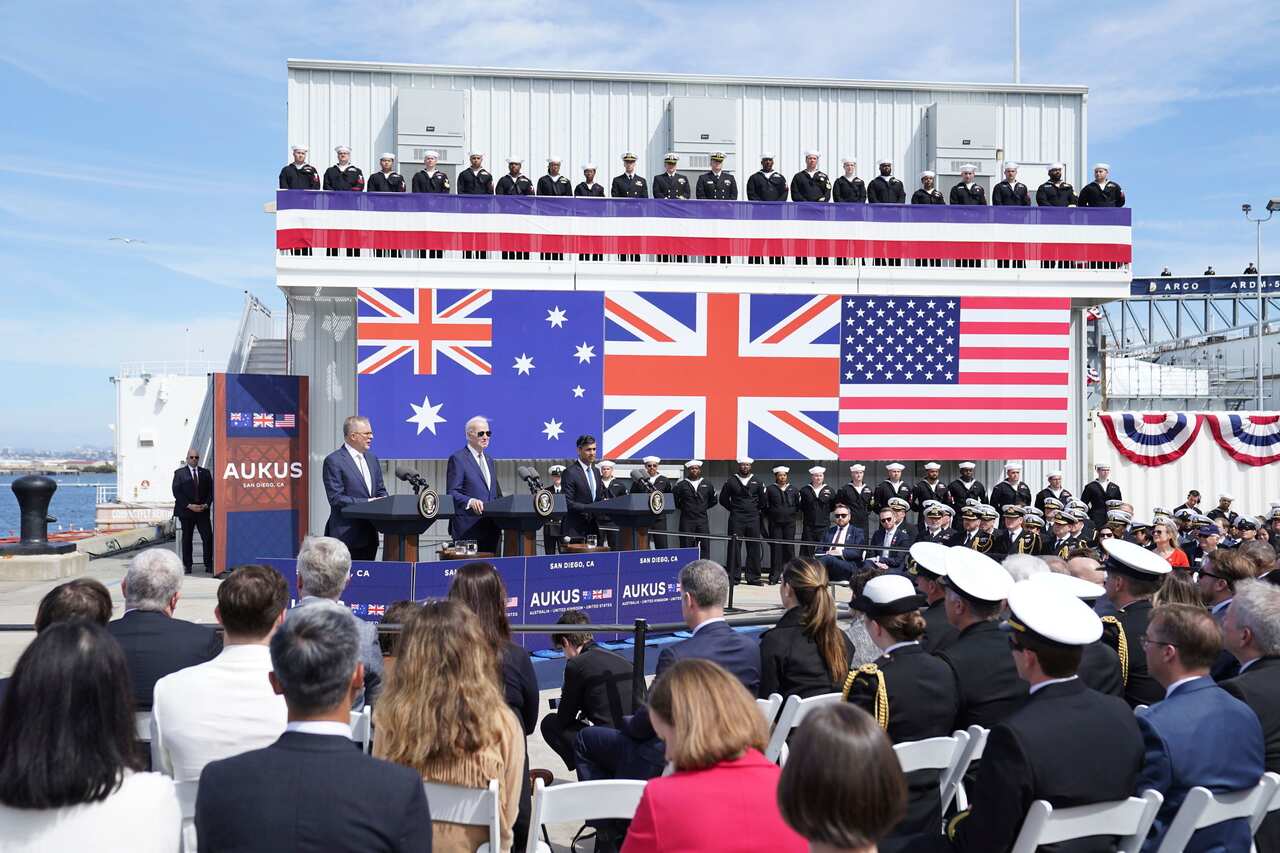 The three leaders standing in front of Australian, UK and US flags.