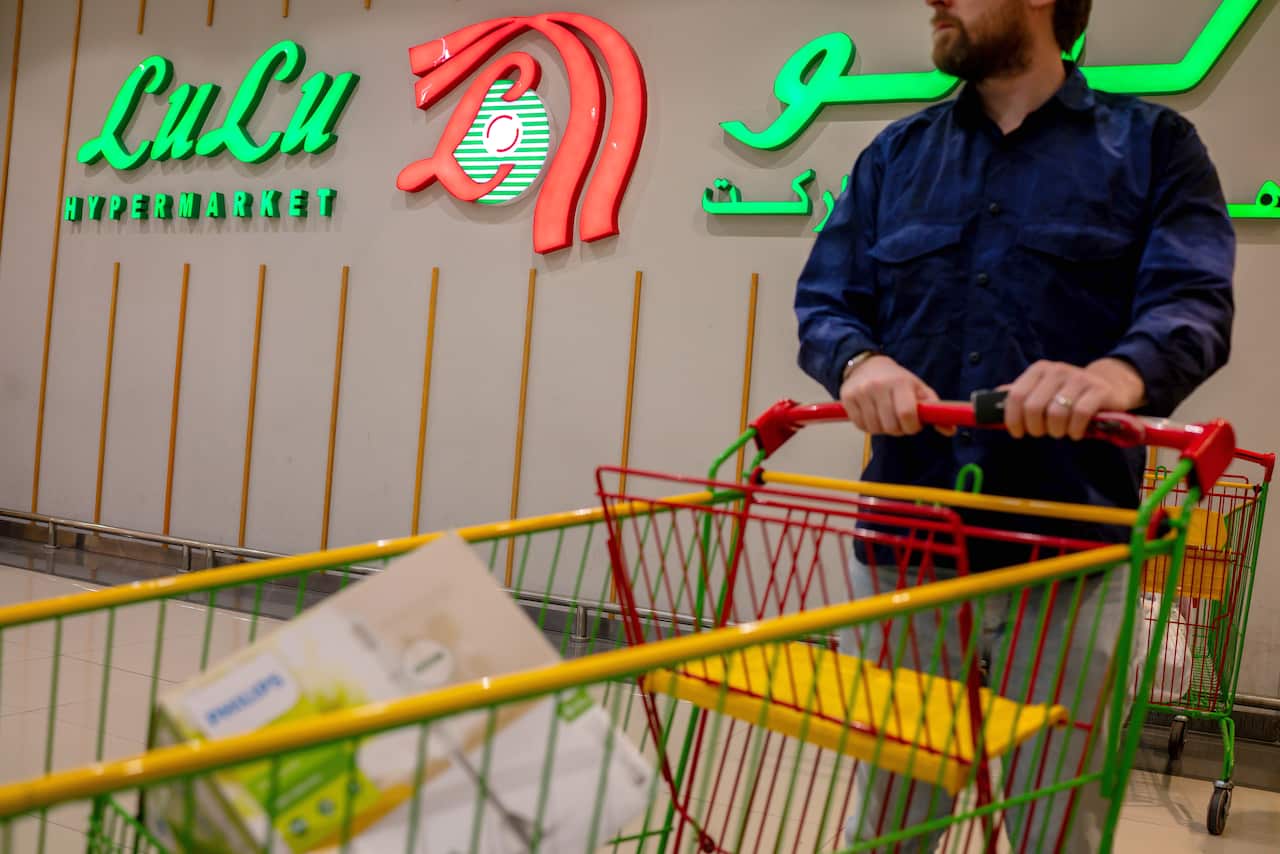 A person pushing a trolley with a Lulu Supermarket sign in the background.