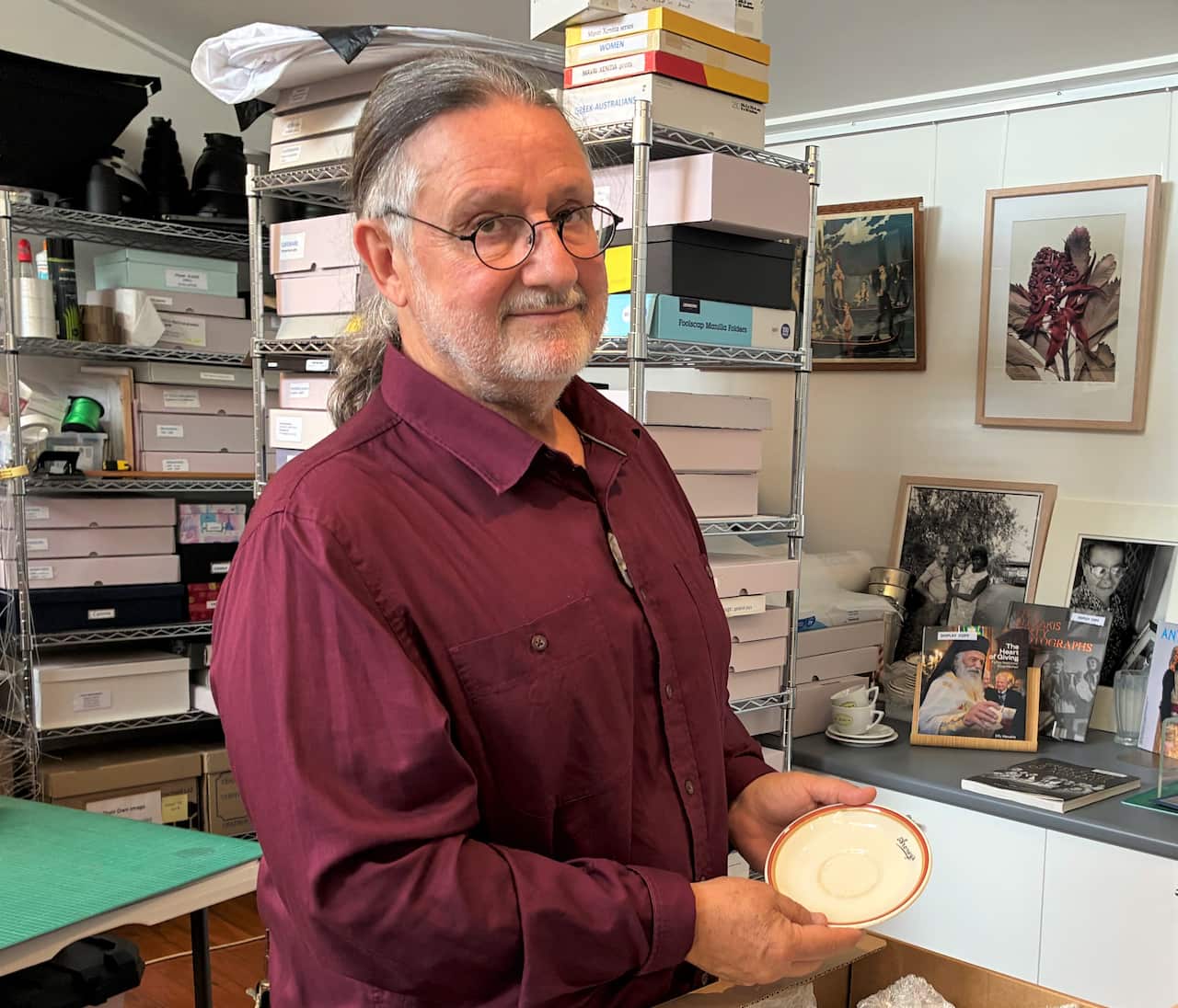 A man in a burgundy shirt stands in a studio holding a small plate.