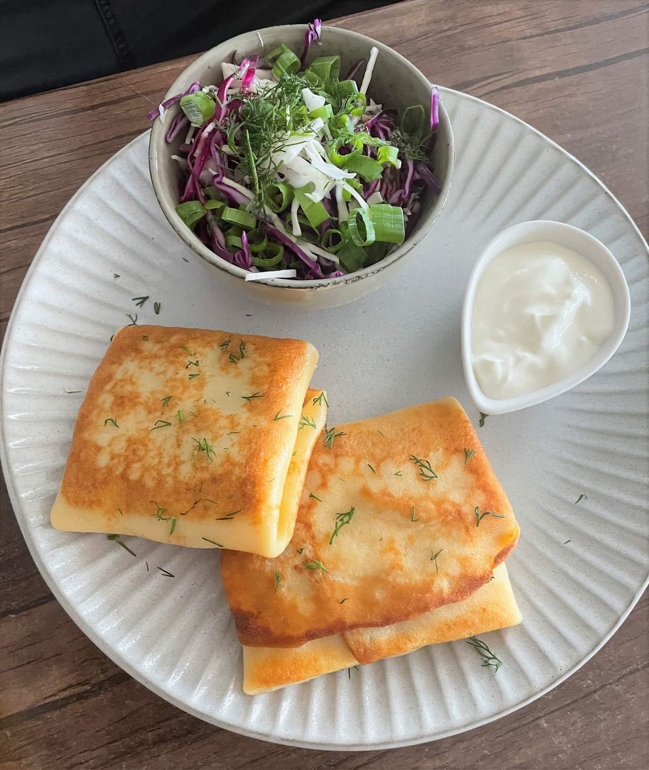 A traditional Ukrainian dish of meat filled crepes on a white plate with a bowl of salad and a bowl of white sauce