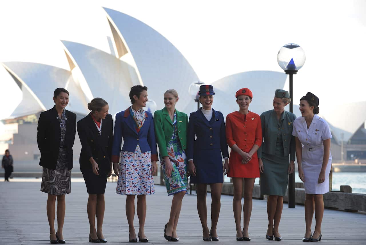 Eight women side by side wearing vintage flight attendant uniforms.