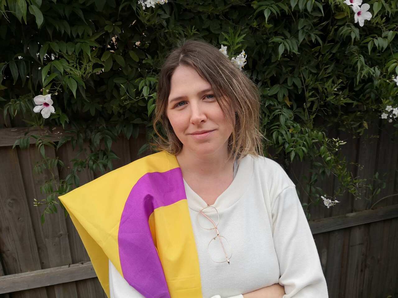 A woman in a white shirt with a purple and yellow flag draped over her shoulder.