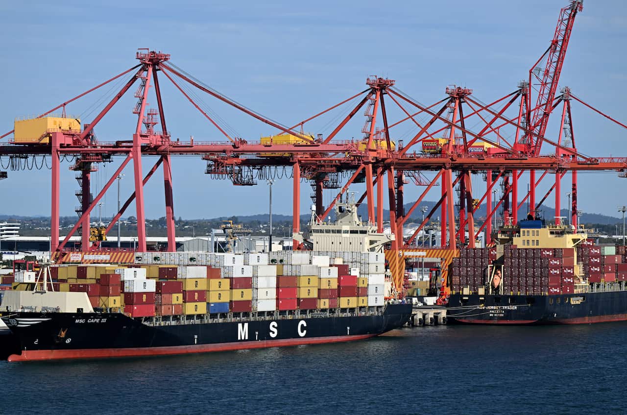 Cargo ships stacked with continers and cranes above them in front of a blue sky