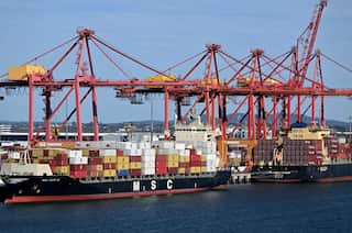 Cargo ships stacked with continers and cranes above them in front of a blue sky