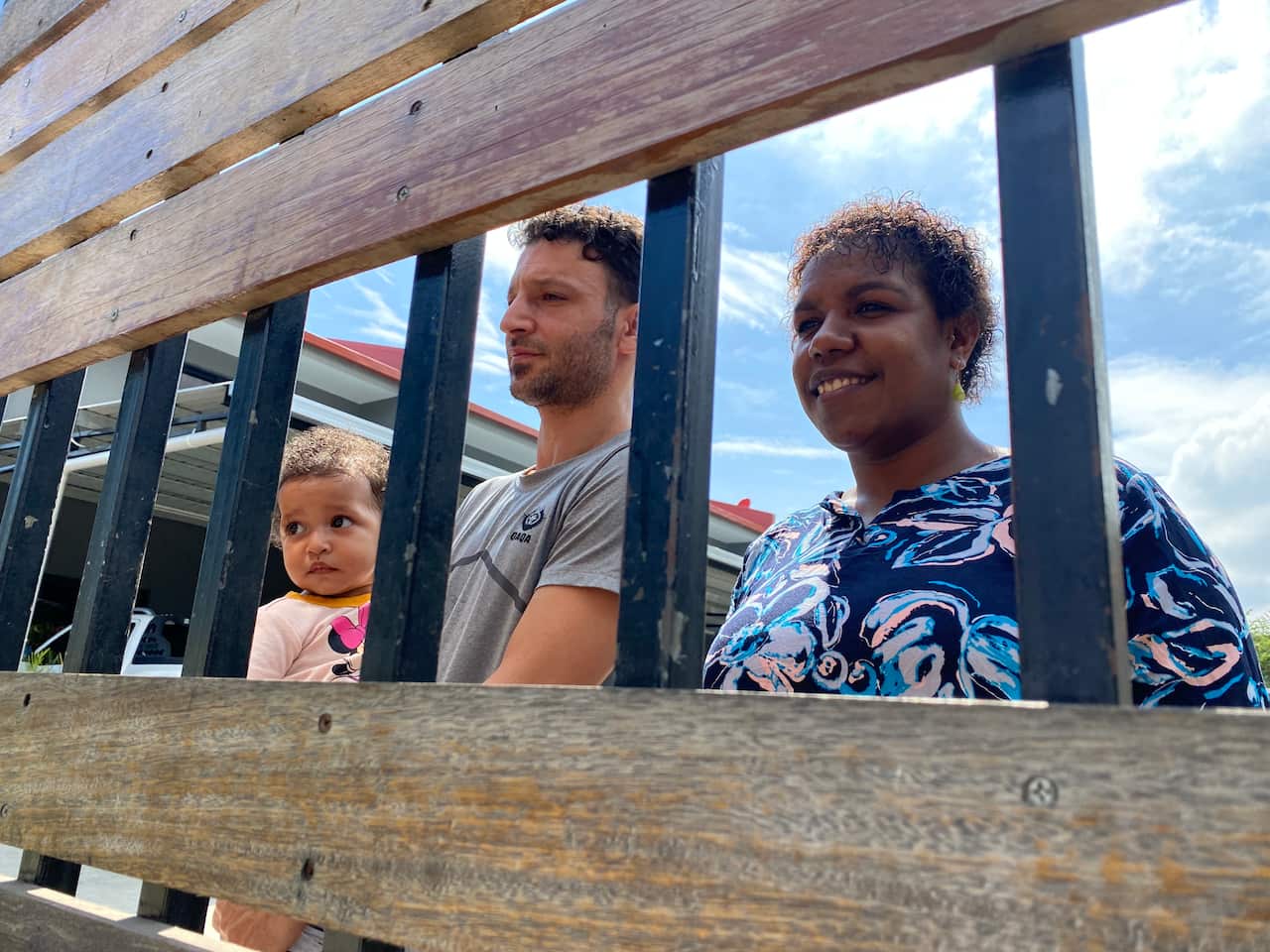 View through a steel gate of a man holding a baby and standing next to a woman