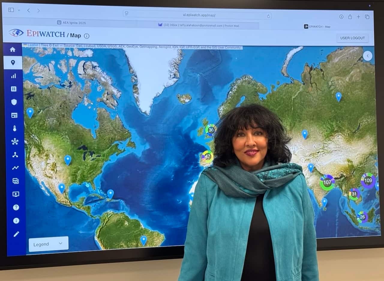 A woman stands in front of a large screen, showing the map of the world.