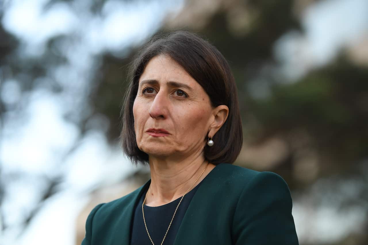 A woman with short black hair, wearing a green blazer, standing outside.