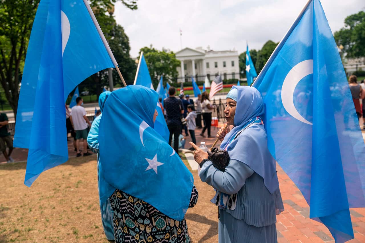 Two women hold the blue flags of East Turkistan.