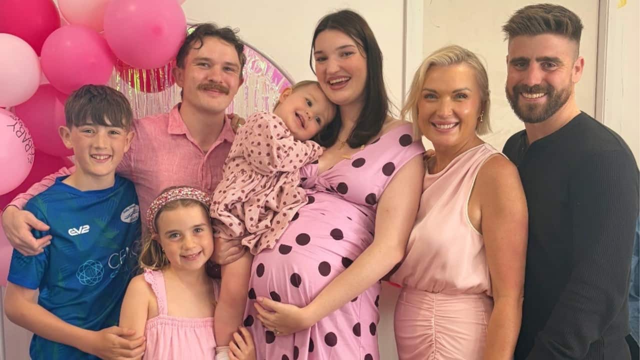 a family portrait of seven family members dressed in pink with pink balloons in the background
