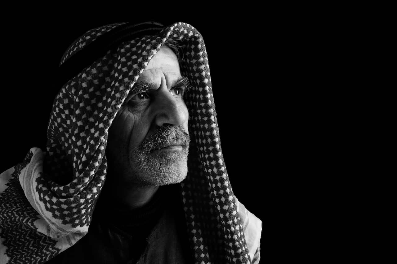 Portrait of sheik in keffiyeh and headscarf on black background