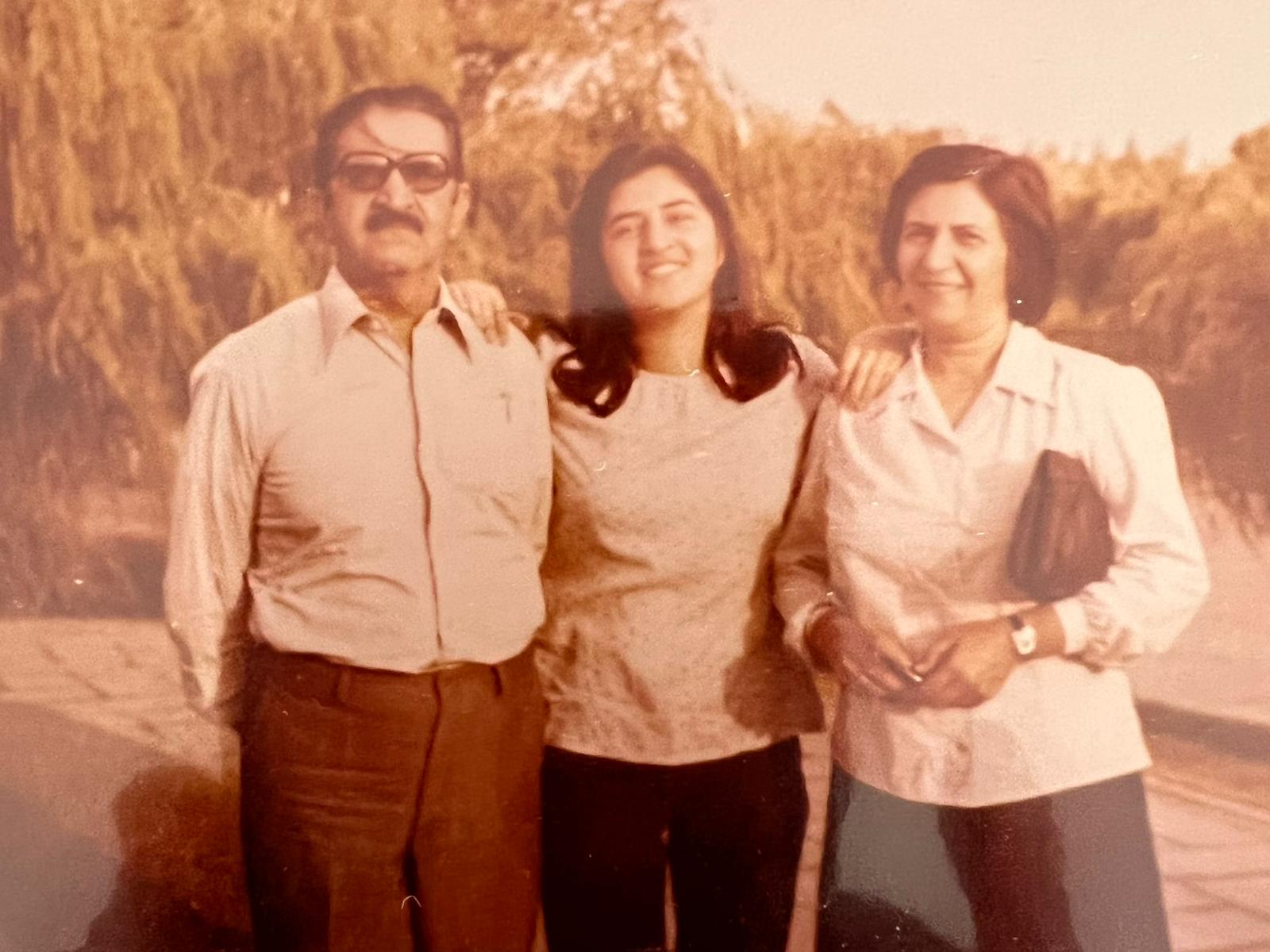  three individuals standing together outdoors: a man on the left, a woman in the center, and another woman on the right, all smiling warmly.