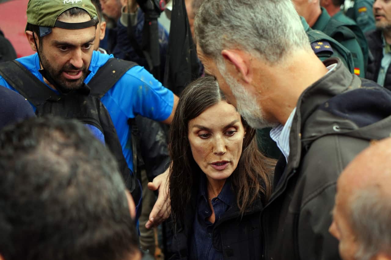 A woman with mud stains on her face talks to a man with other people surrounding them.