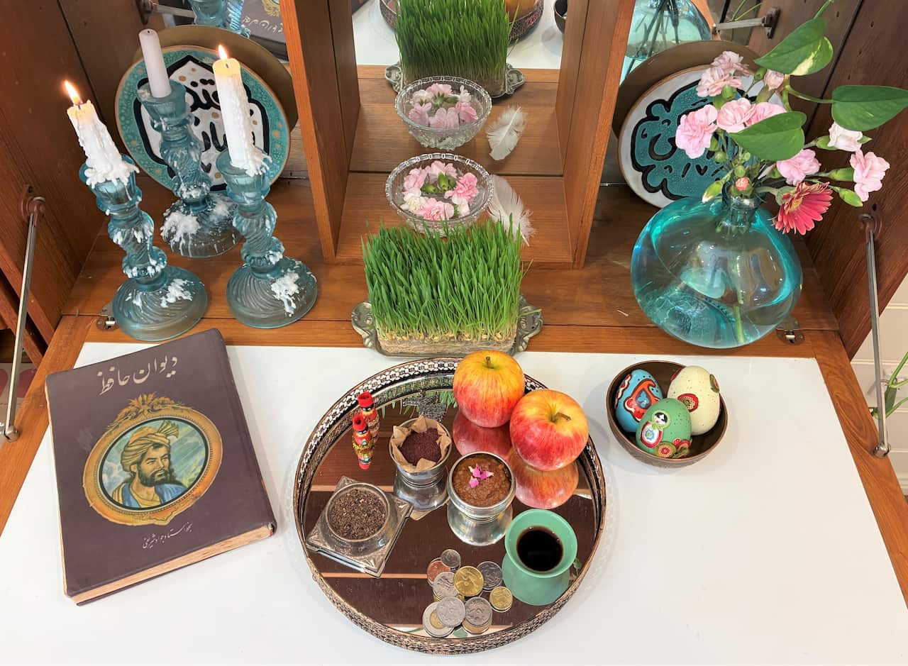 A table laden with items including apples, wheatgrass, small dishes of spices and lit candles.