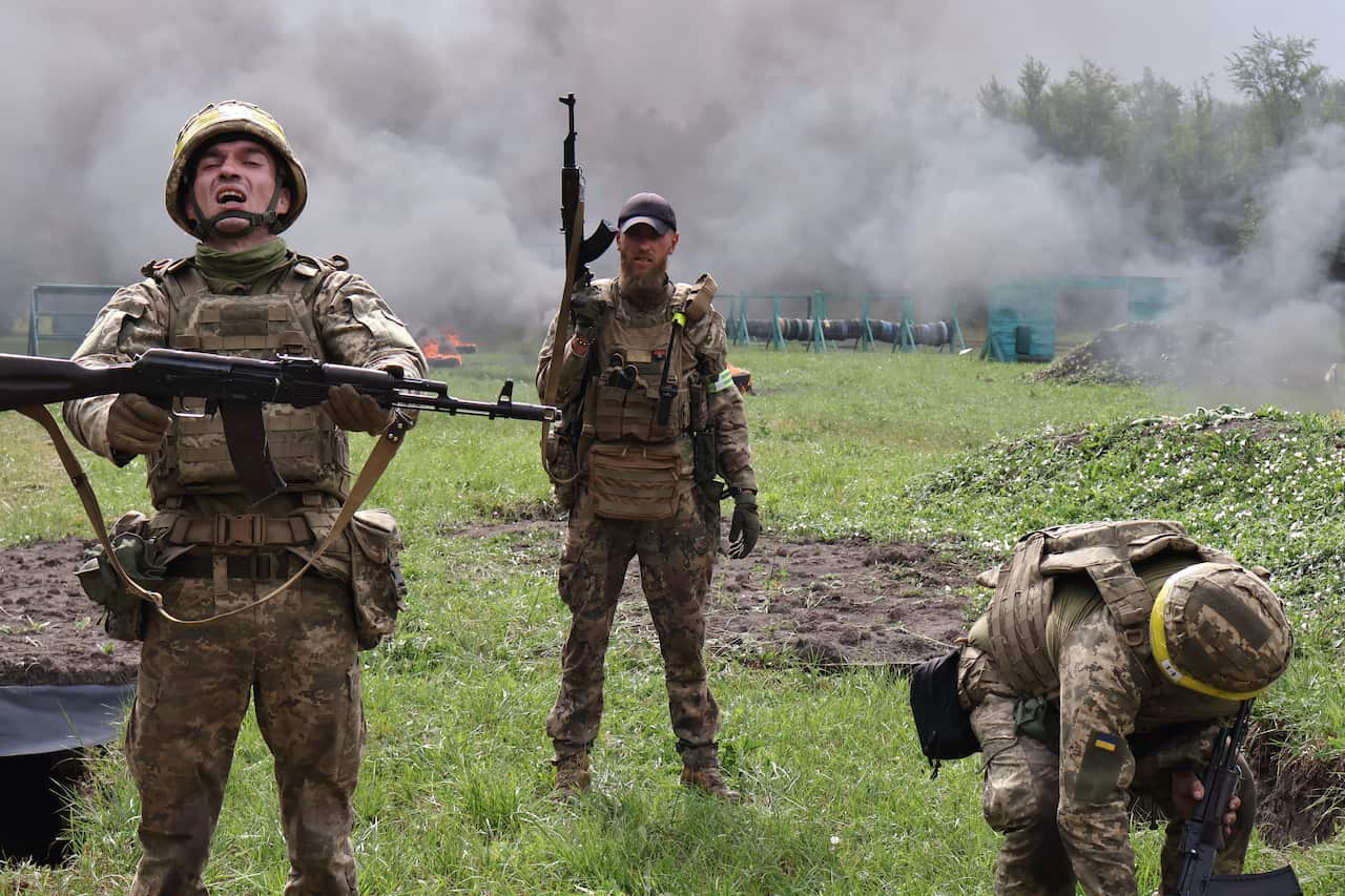 Soldiers wearing a camouflage uniform hold guns during training while grey smoke fills the background.