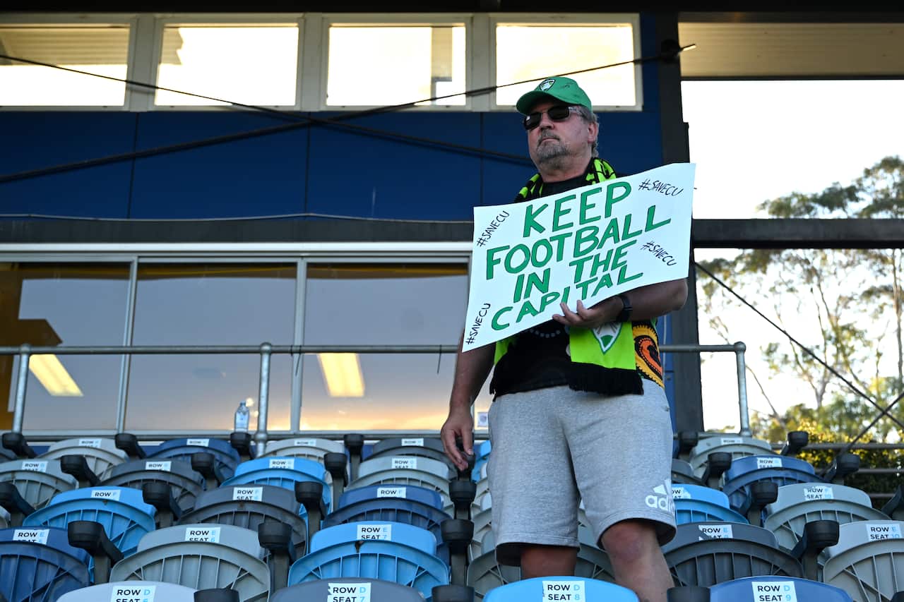 A man holding a sign in a stadium holding a sign that reads "keep football in the capital"