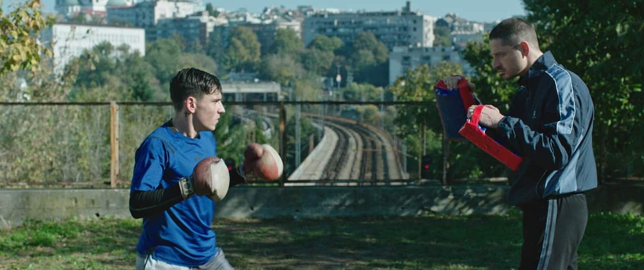 A young man with boxing gloves is training with an older man, his sparring partner, outdoors during the day.jpeg