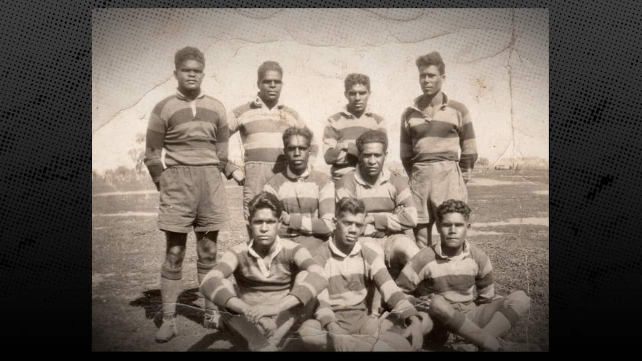 Early black and white team photo of nine members of the Wiradjuri Erambie All Blacks in stripped rugby jerseys, with three players sitting at the front, two kneeling behind, and four standing at the back.