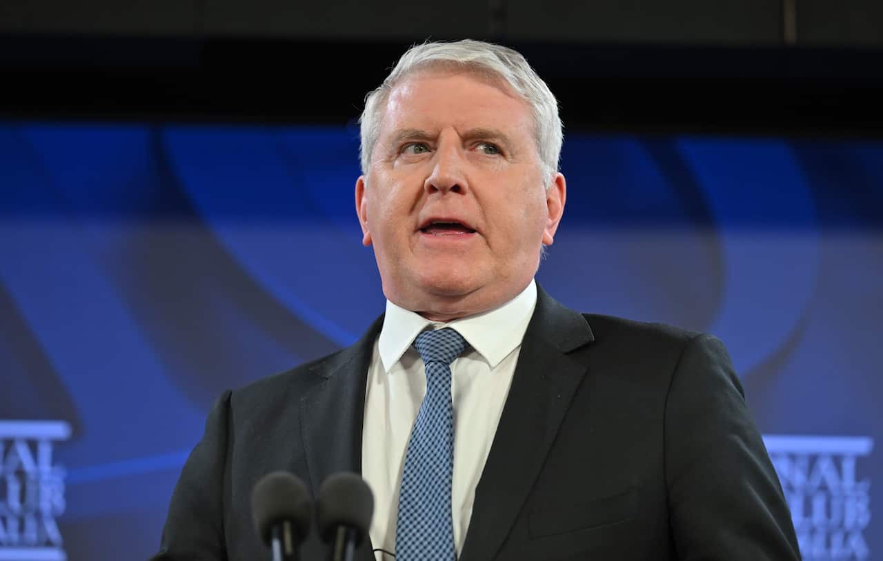 A man in a suit speaking at a podium in front of a blue background.