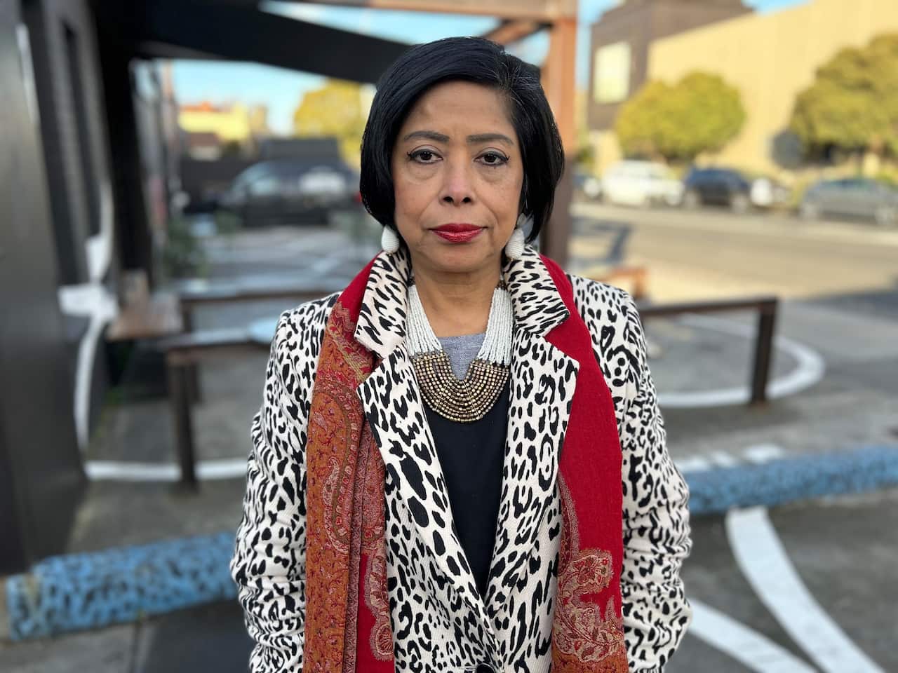  Manorani Guy wearing a black and white jacket with a red scarf standing on a Melbourne street.