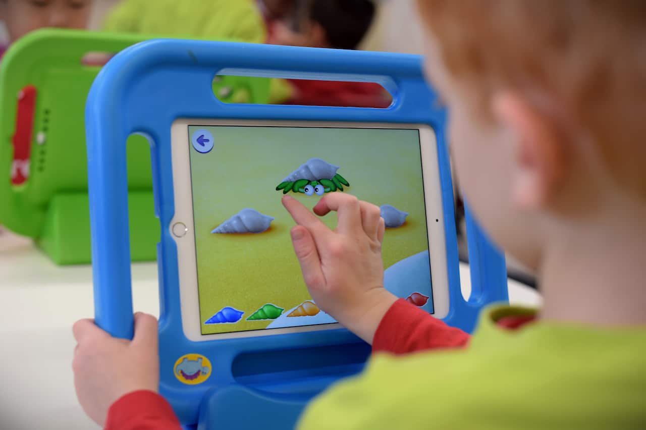 A young boy with red hair taps on the screen of an iPad.
