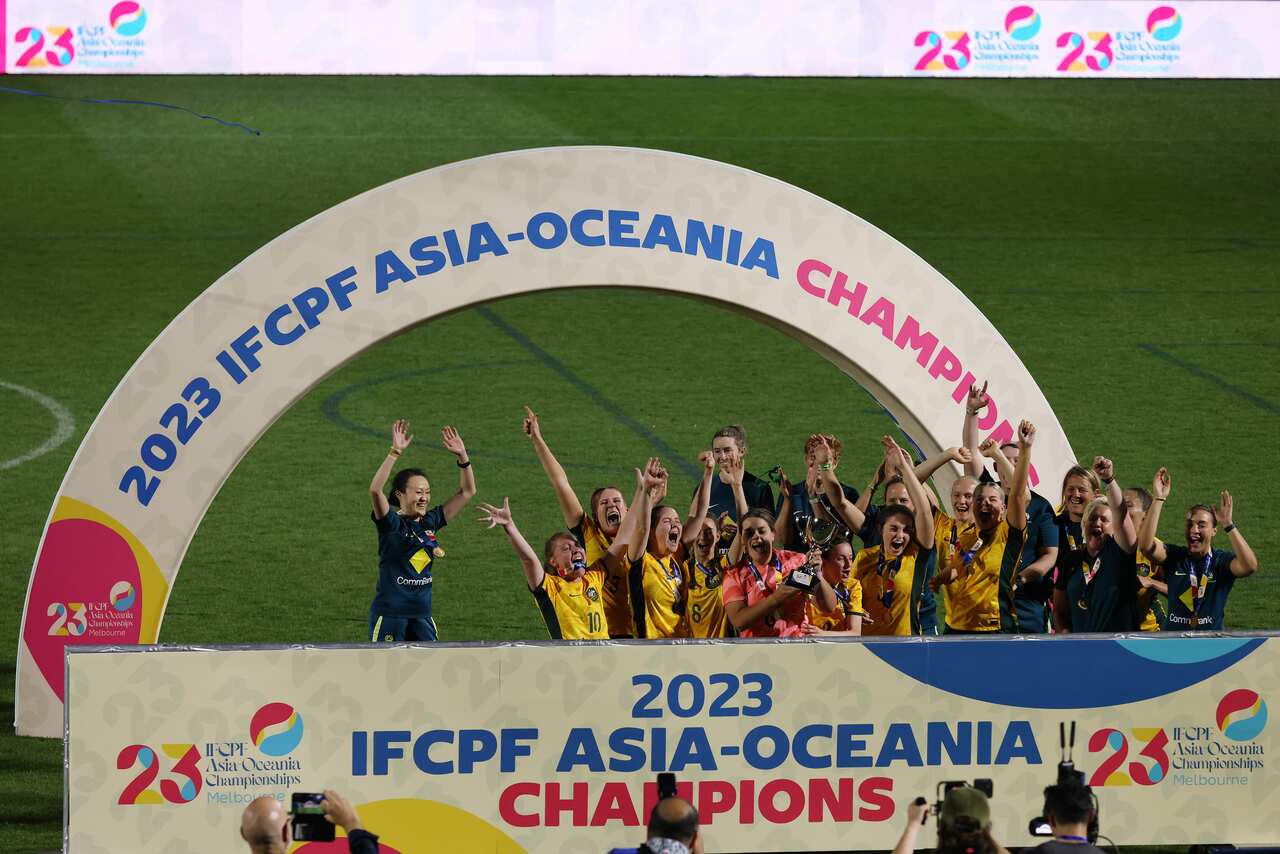 A group of women's football players celebrate victory on a pitch. 