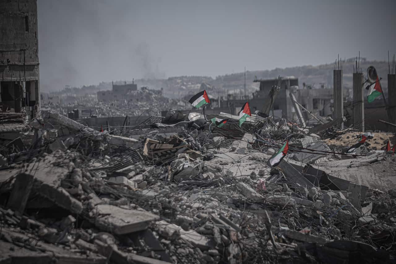 Palestinian flags raised amid grey wreckage and the rubble of heavily damaged buildings.