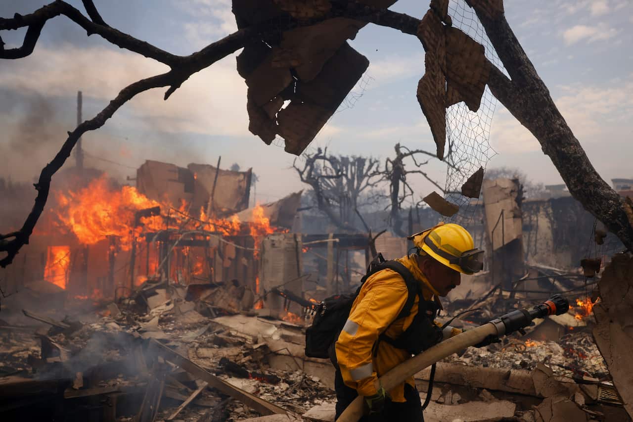 A firefighter uses a hose to extinguish flames around a charred structure.