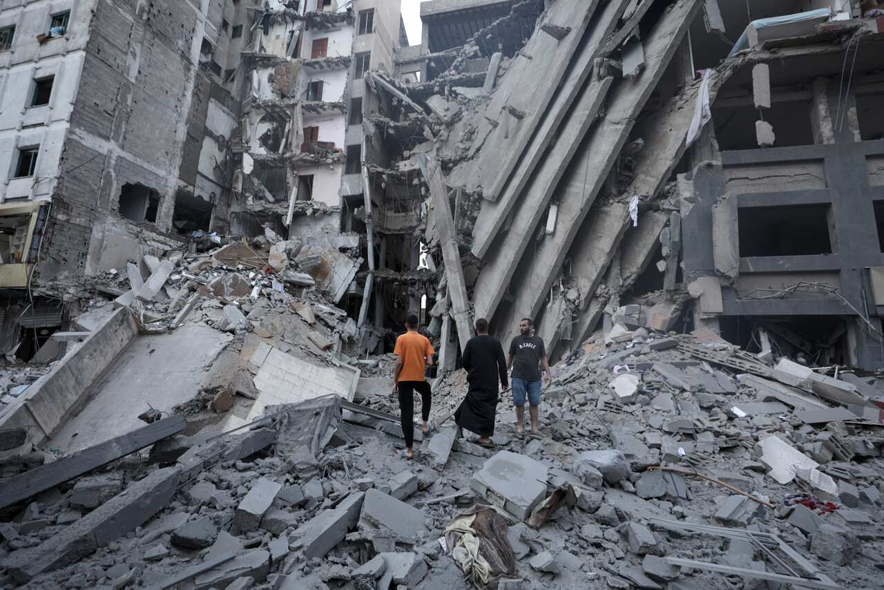 Three Palestinian men inspect the rubble of a destroyed building.