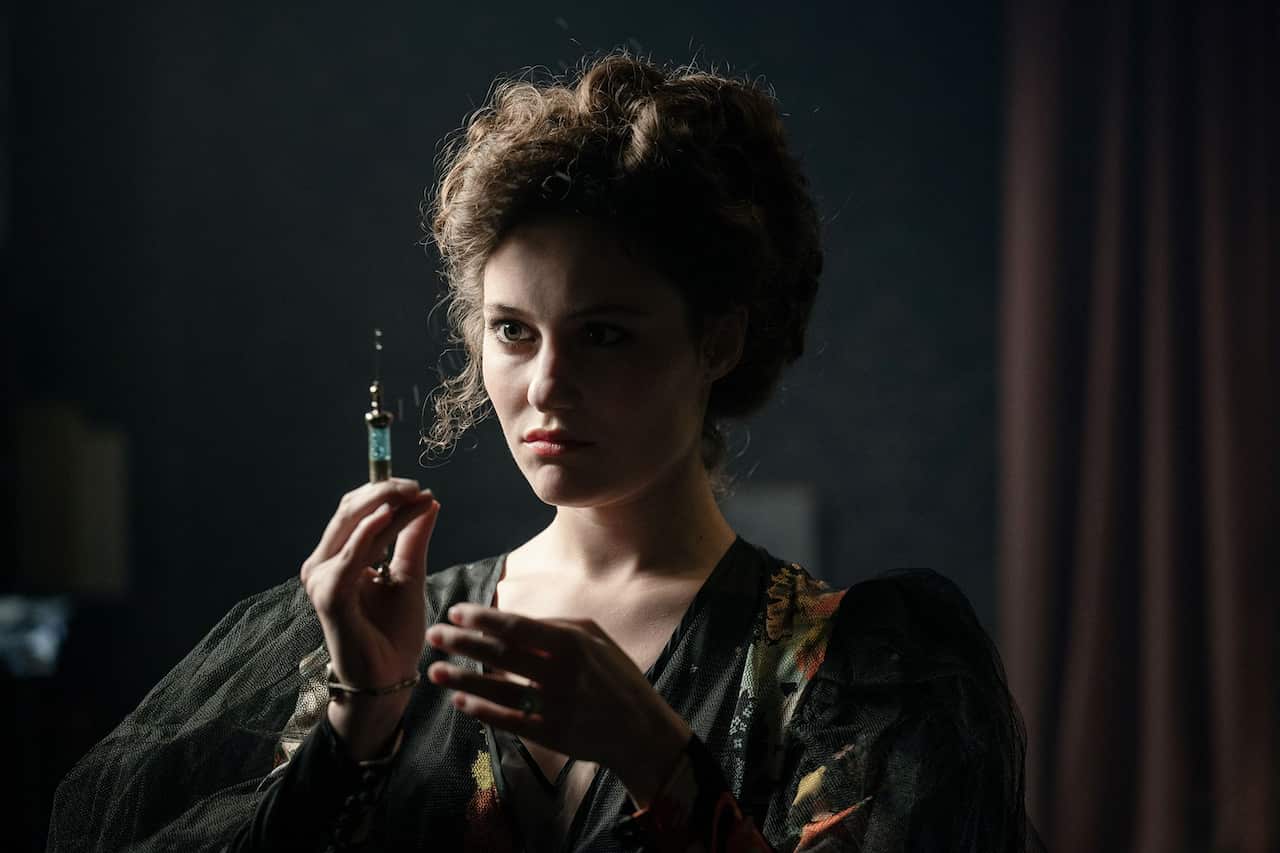 A woman in 1900s dress holds up and stares at a needle