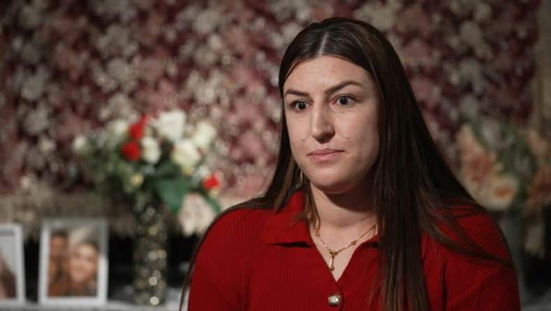 A woman wearing a red shirt looks forward with a serious expression on her face. 