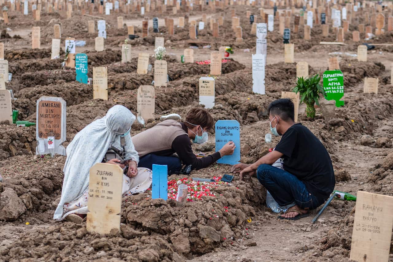 Three people wearing face masks gather around a tombstone.